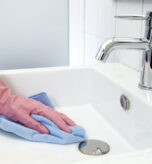 The woman, who is cleaning the washbasin with microfiber cloth and gloves