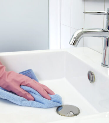 The woman, who is cleaning the washbasin with microfiber cloth and gloves
