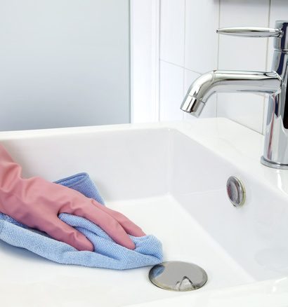 The woman, who is cleaning the washbasin with microfiber cloth and gloves