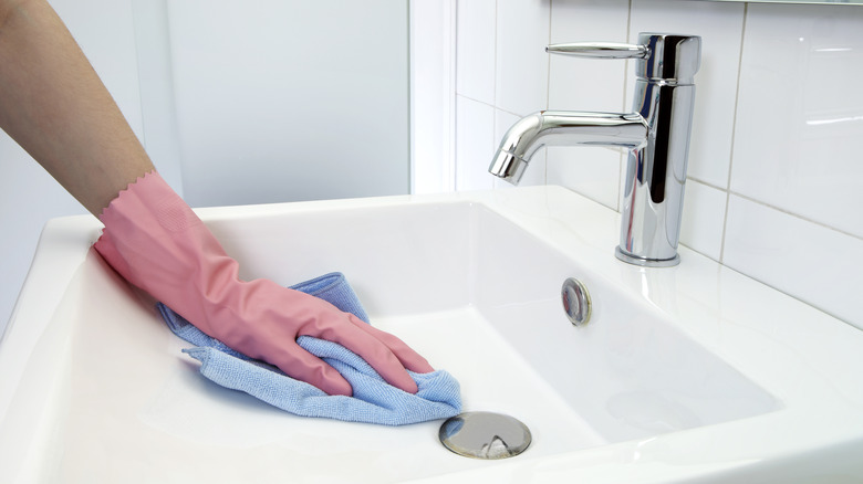The woman, who is cleaning the washbasin with microfiber cloth and gloves